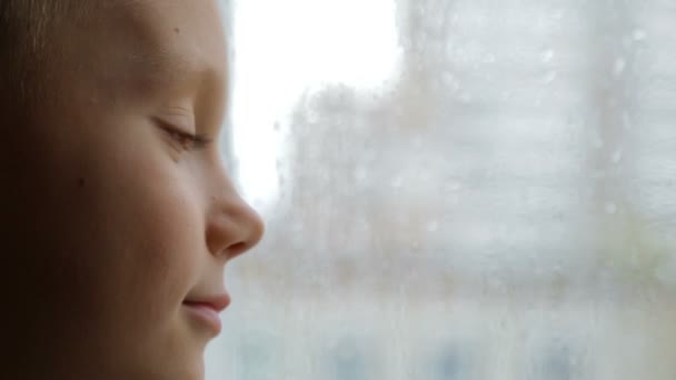 Üzgün çocuk yağmurlu havalarda pencereden görünüyor — Stok video
