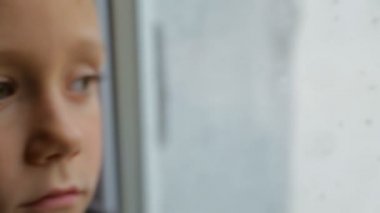 Üzgün çocuk yağmurlu havalarda pencereden görünüyor
