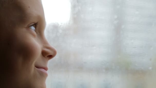 Triste garçon regarde par la fenêtre par temps pluvieux — Video