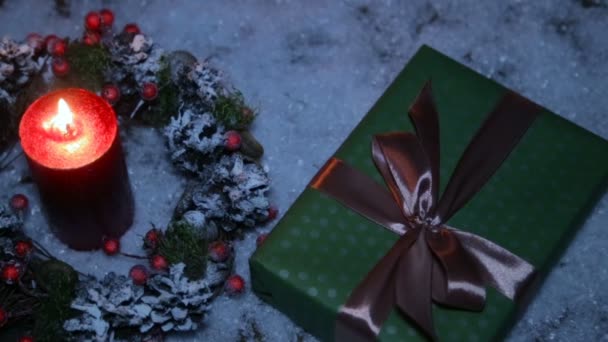 Regalo de Navidad con una cinta marrón en el fondo de nieve artificial y una vela encendida — Vídeo de stock