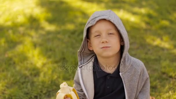 A boy is eating a fresh banana in a summer park — Stock Video