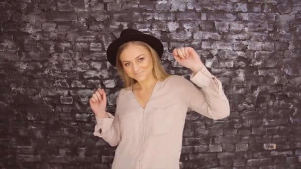 Una chica con un sombrero negro está bailando sobre el fondo de una pared texturizada — Vídeo de stock