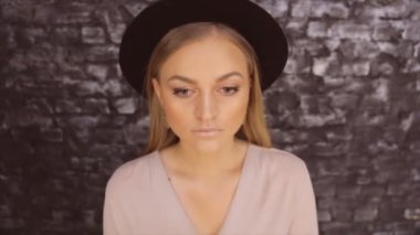 Bir kız siyah bir şapka ve bir tuğla duvar arka planda poz bir gri gömlek