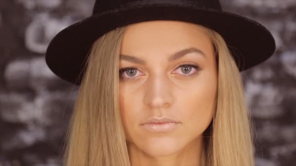 Portréja egy szőke fekete kalapot ellen egy téglafal háttér — Stock videók