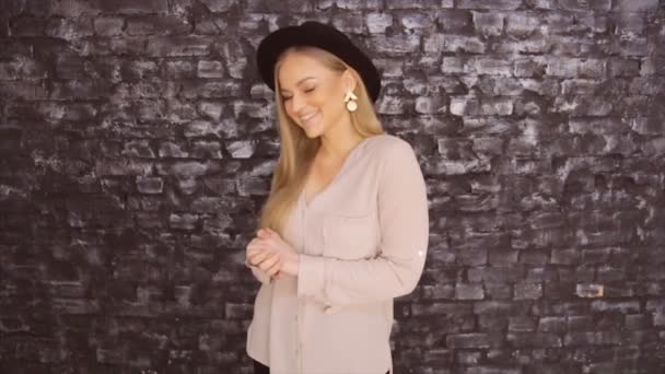 Modell i en svart hatt och en grå tröja poserar mot tegel vägg bakgrund — Stockvideo