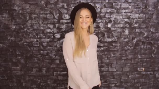 Modelo en sombrero negro y camisa gris posando sobre un fondo de pared de ladrillo — Vídeo de stock