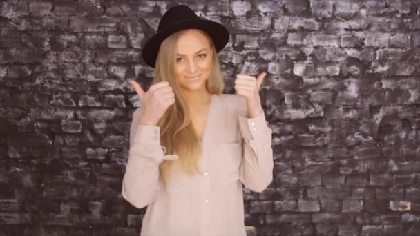 Modell i en svart hatt och en grå tröja poserar mot tegel vägg bakgrund — Stockvideo