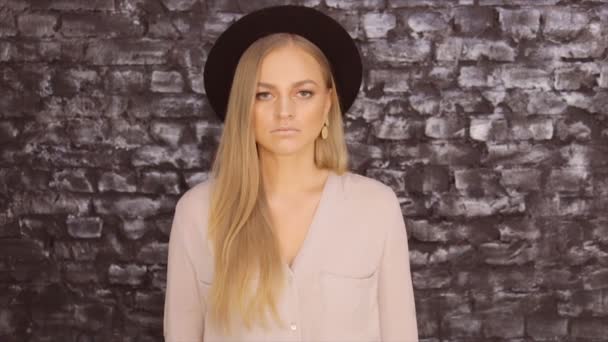 Une fille avec un chapeau noir et une chemise grise posant sur un fond de mur de briques — Video