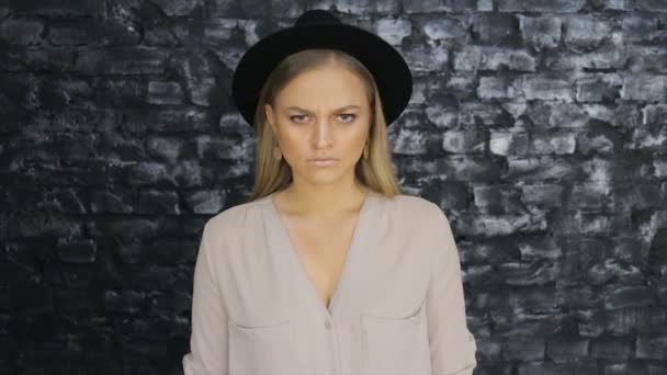 Девушка в черной шляпе и серой рубашке, позирующей на фоне кирпичной стены — стоковое видео