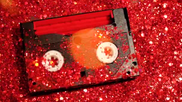 Black video cassette on the background of red glitter — Stock Video