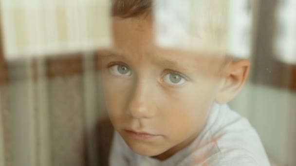 Un niño triste mira por la ventana — Vídeos de Stock