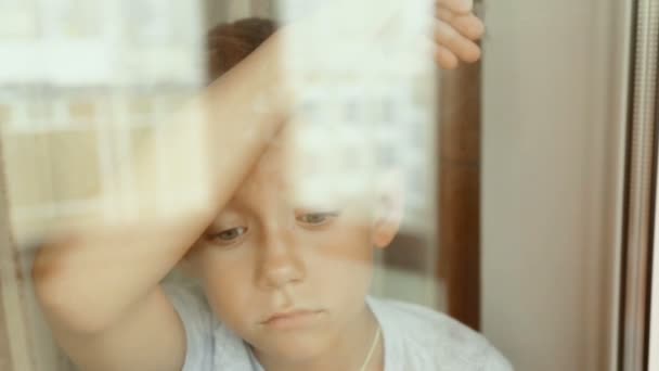 Un niño triste mira por la ventana — Vídeo de stock