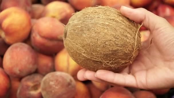 Кокос в женской руке на фоне свежих персиков — стоковое видео