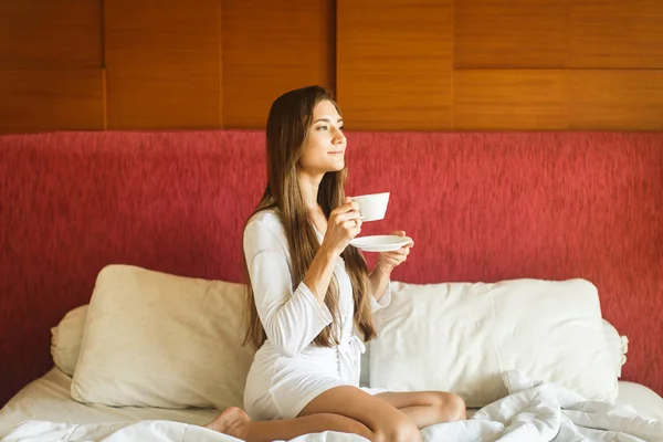 Joven en bata blanca bebiendo té en la cama —  Fotos de Stock