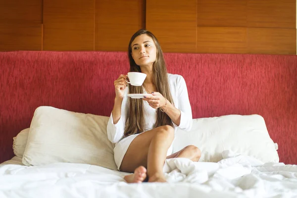 Joven en bata blanca bebiendo té en la cama —  Fotos de Stock