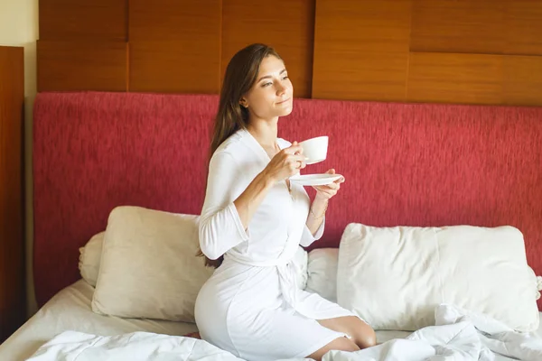 Joven en bata blanca bebiendo té en la cama —  Fotos de Stock