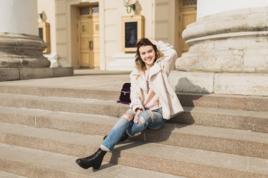 Genç güzel kız tiyatronun basamaklarında oturur