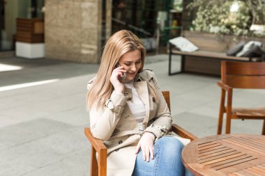  elinde bir telefon ile bir masada oturan kız