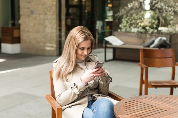 Chica sentada en una mesa con un teléfono en las manos — Foto de Stock