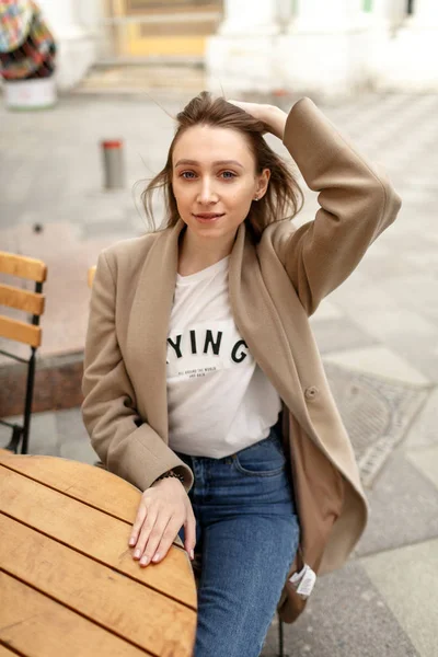 Mujer joven está sentada a la mesa en un café en la calle —  Fotos de Stock