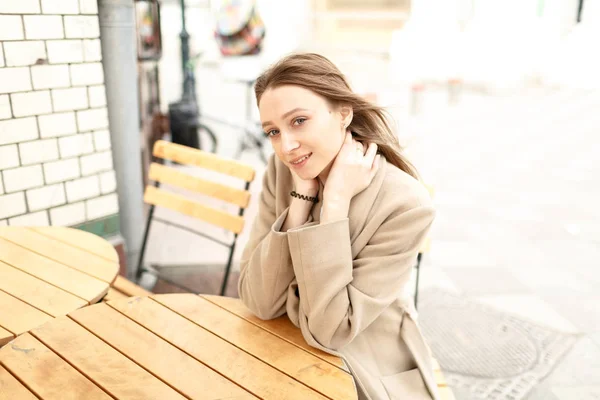 Mujer joven está sentada a la mesa en un café en la calle —  Fotos de Stock
