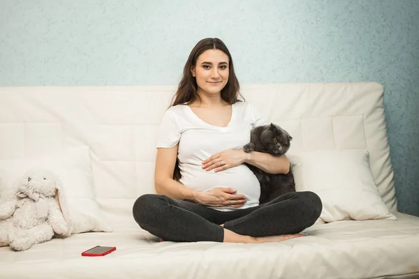 Femeie gravidă cu pisică pe canapea albă — Fotografie, imagine de stoc