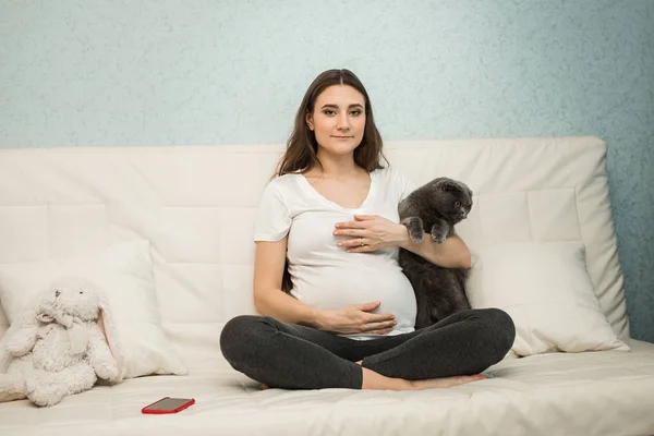 Femeie gravidă cu pisică pe canapea albă — Fotografie, imagine de stoc