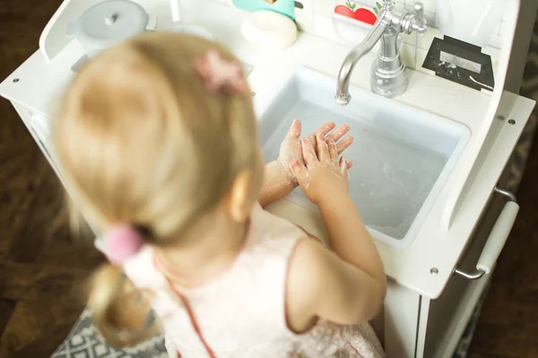 little girl washes her hands with soap in the children\'s kitchen. hand hygiene rules concept