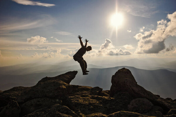 Турист с рюкзаком прыгает через скалы закат неба на заднем плане
