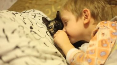 Tv izlerken kedi ile yatakta yatan küçük çocuk