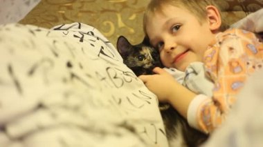 Tv izlerken kedi ile yatakta yatan küçük çocuk