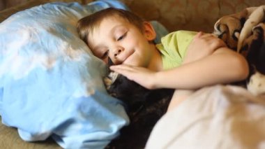 Tv izlerken kedi ile yatakta yatan küçük çocuk