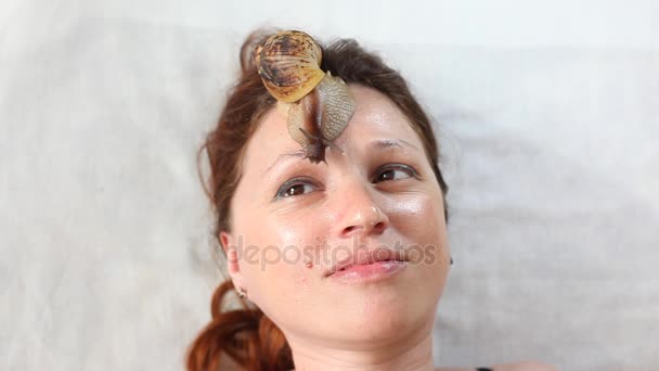 Una joven en el spa recibe un masaje facial con caracoles africanos Achatina. Los caracoles comen la piel muerta de los producidos. Al final, deja la piel suave y fresca . — Vídeos de Stock