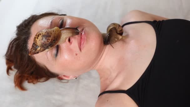 Una joven en el spa recibe un masaje facial con caracoles africanos Achatina. Los caracoles comen la piel muerta de los producidos. Al final, deja la piel suave y fresca . — Vídeo de stock