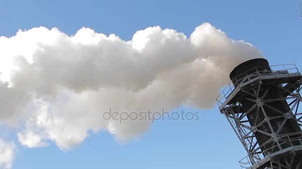 Белый дым идет из труб завода против голубого неба — стоковое видео