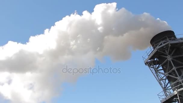 Белый дым идет из труб завода против голубого неба — стоковое видео