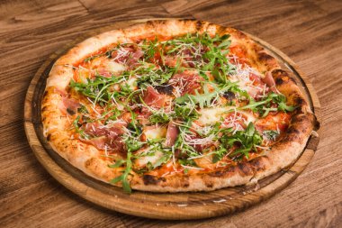 Etli pizza, pastırma, ahşap arka planda roka.