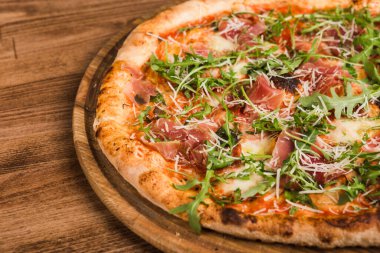 Etli pizza, pastırma, ahşap arka planda roka.