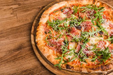 Etli pizza, pastırma, ahşap arka planda roka.