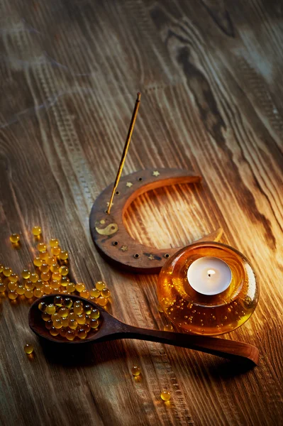 Κερί σε κίτρινο γυάλινο κηροπήγιο με φυσαλίδες αέρα στο εσωτερικό, θυμίαμα κολλήσει κάπνισμα, κάψουλες ιχθυελαίου — Φωτογραφία Αρχείου
