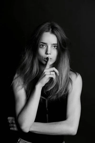 La chica con el pelo largo sostiene el dedo cerca de los labios. gesto de silencio, secreto, secreto —  Fotos de Stock