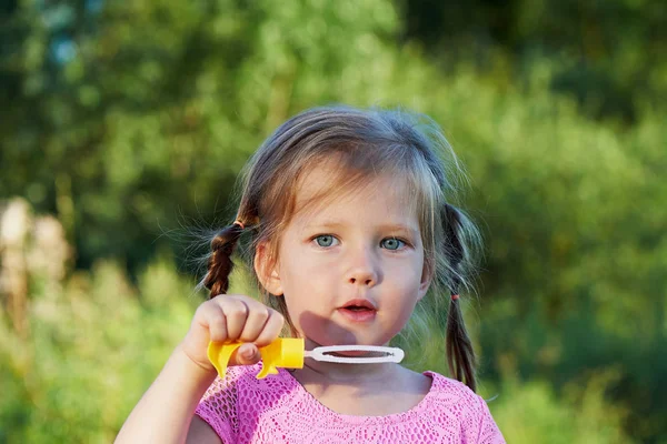 La chica en el vestido rosa de 3 años y dos trenzas disfruta de la vida, inflando burbujas. Joy. —  Fotos de Stock