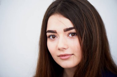 Genç kız kameraya bakıyor. Uzun siyah saçlı ve kahverengi gözleri .