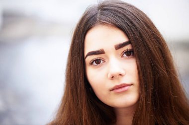 Genç kız kameraya bakıyor. Uzun siyah saçlı ve kahverengi gözleri .