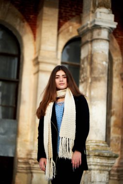 Genç kız kameraya bakıyor. Uzun siyah saçlı, eşarp, beyaz tıknaz örme.