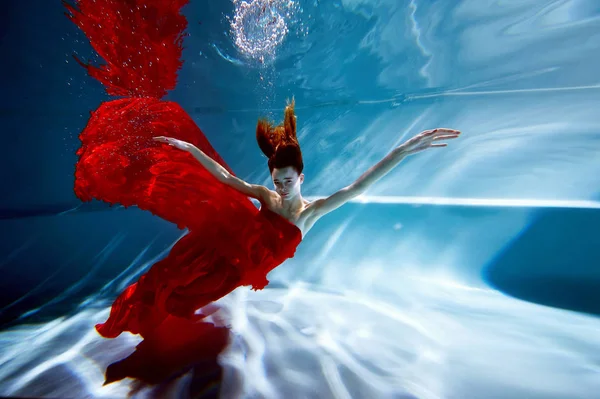 Saf su ile havuzunda sualtı. Güzel genç kız bir kırmızı elbise ve akan saç. — Stok fotoğraf