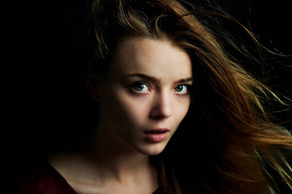 Beautiful girl looks piercing eyes into the camera. Hair flying. Drama. Studio photography in low key on a dark background