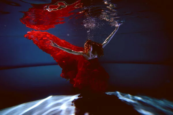 Saf su ile havuzunda sualtı. Güzel genç kız bir kırmızı elbise ve akan saç. — Stok fotoğraf