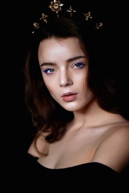 Bir taç şeklinde kafasına bir dekorasyon ile güzel bir kız portresi. Uzun örgülü saç. Karanlık bir arka plan üzerinde bir stüdyoda