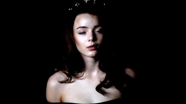 Portret van een prachtig meisje met een decoratie op de kop in de vorm van een kroon. Lang gestrande haren. In een Studio op een donkere achtergrond — Stockvideo